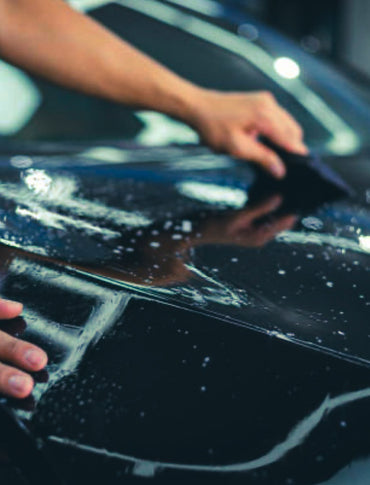 Person applying PPF car wrap to a vehicle in a workshop setting