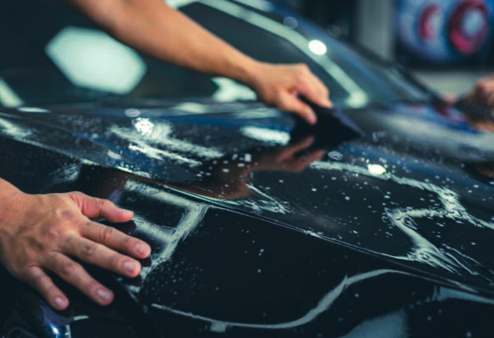 Person applying PPF car wrap to a vehicle in a workshop setting